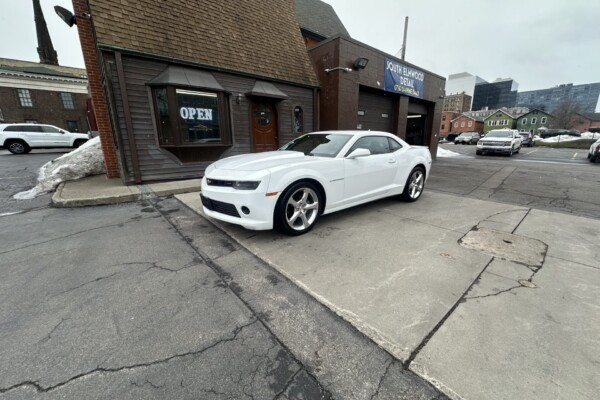 image shows a white 2015 Chevrolet Camaro parked on a concrete surface in front of a building